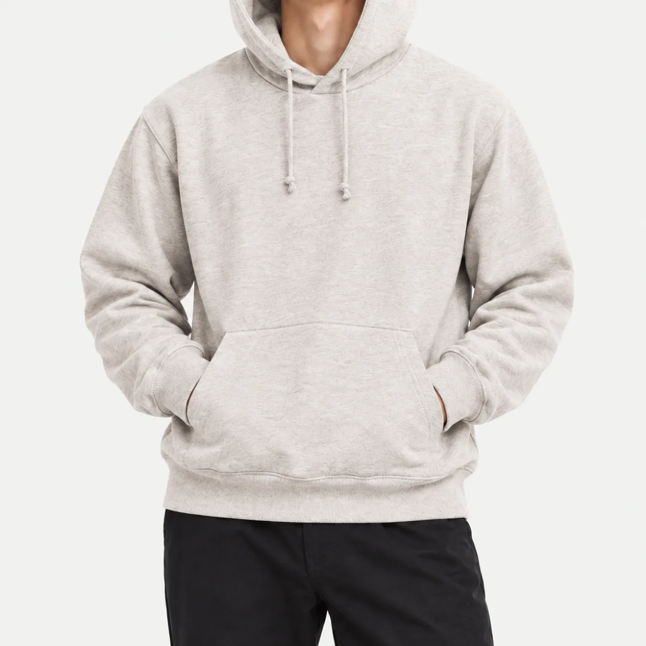A model wearing an oatmeal basic French terry hoodie with hands in the pockets