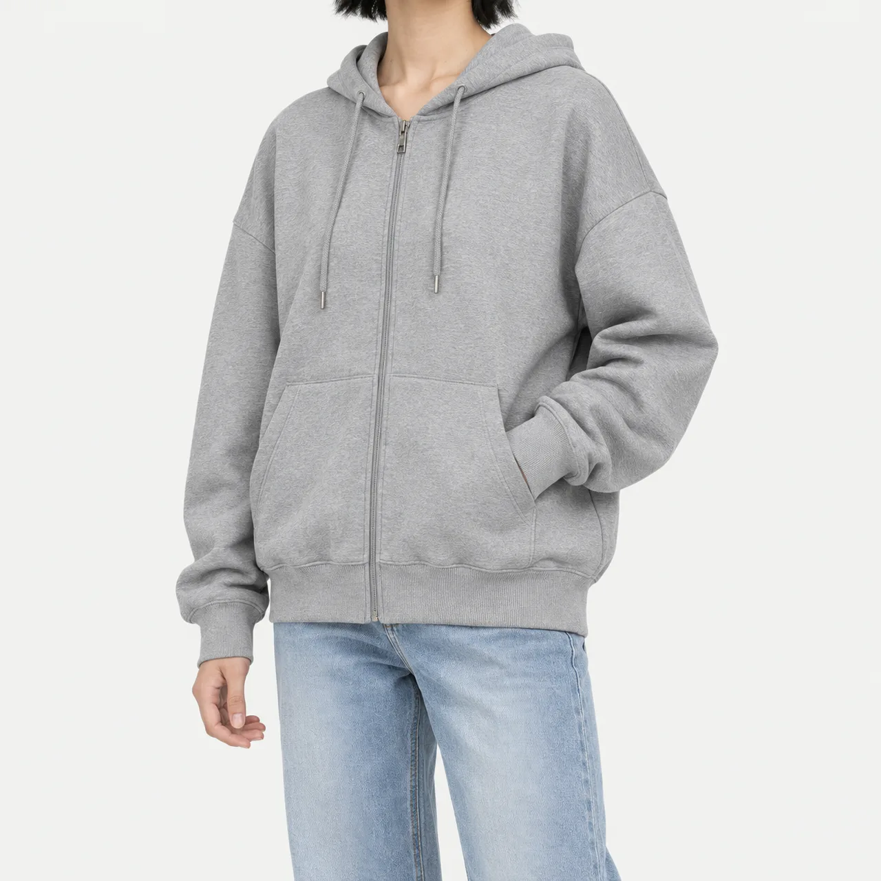 A model wearing a gray oversized light zip-up hoodie with a hand in the pocket