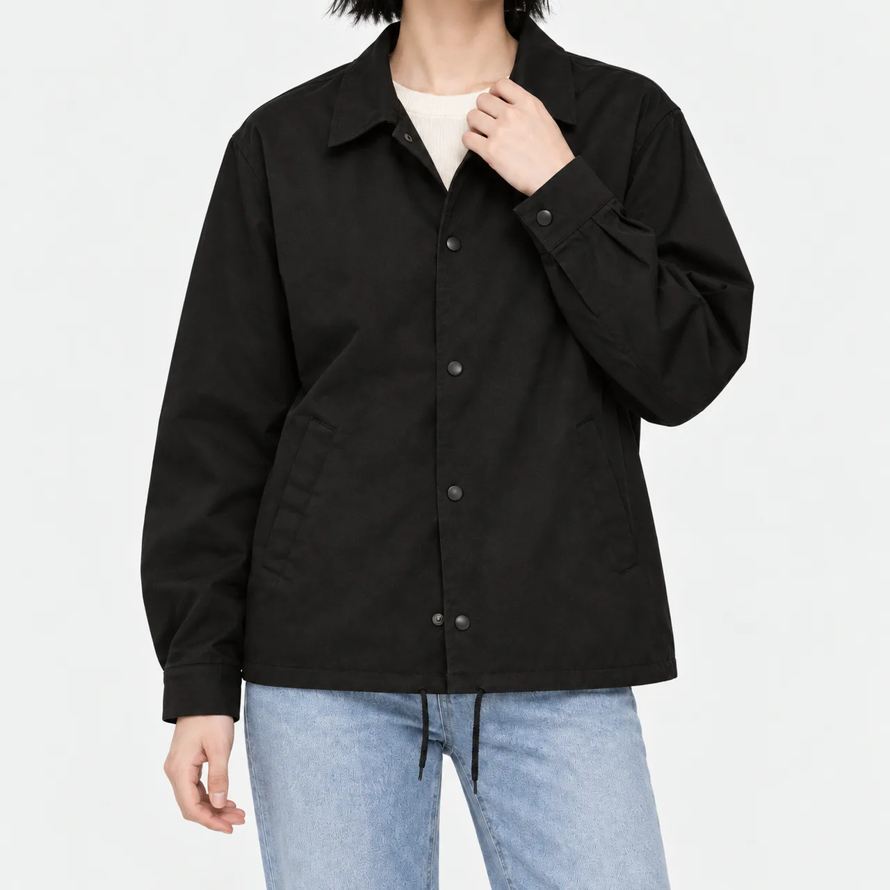 A model wearing a black cotton coach jacket and holding the front placket