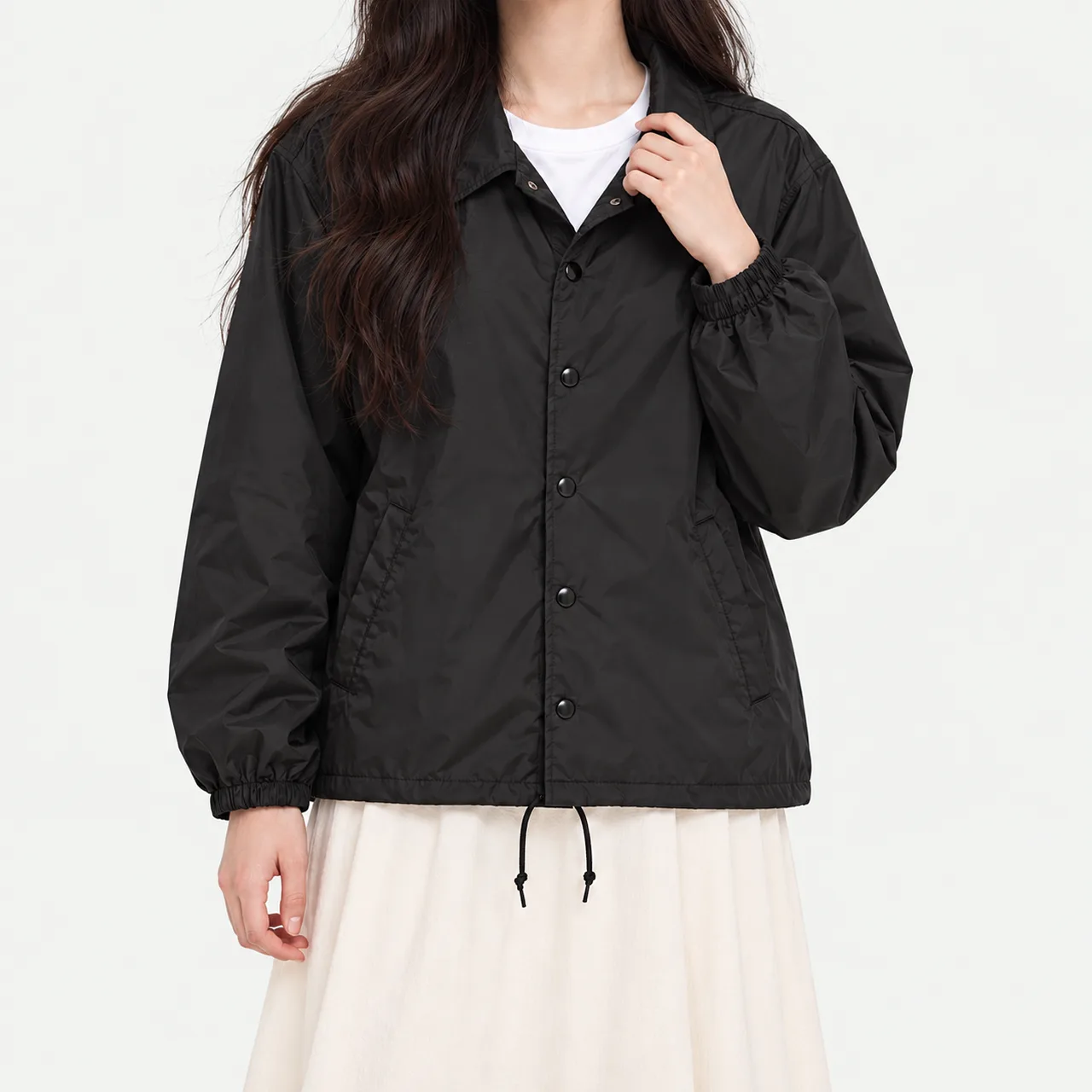 A model wearing a black nylon coach jacket and holding the collar