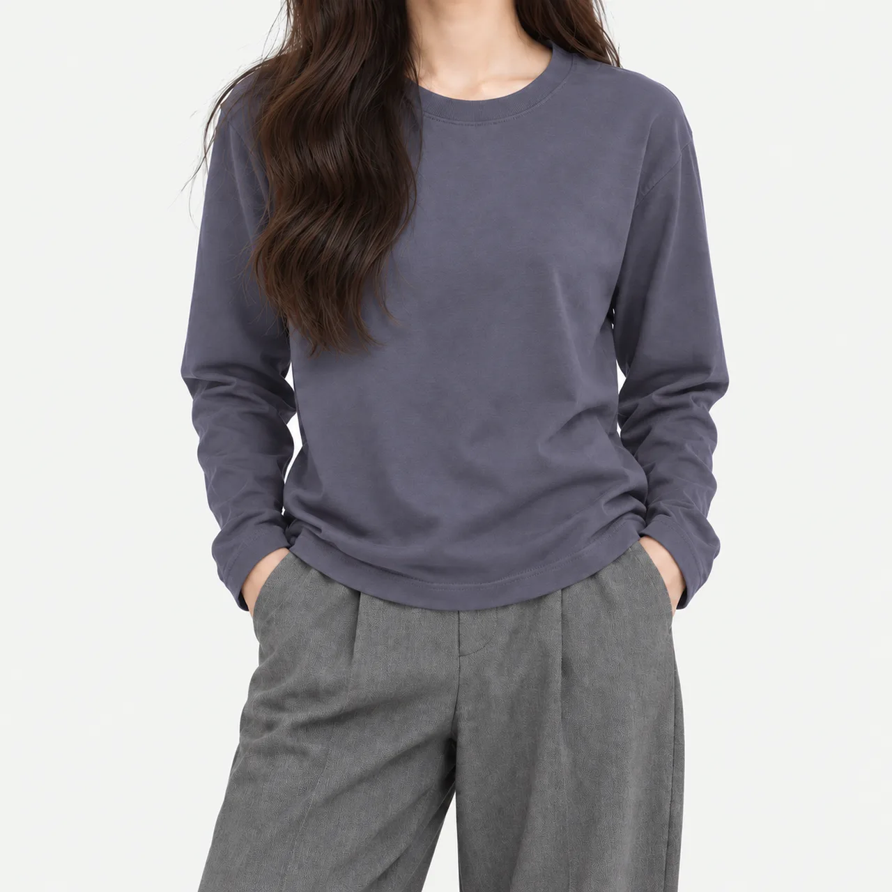 A model wearing a dusty blue basic crewneck long sleeve T-shirt with hands in the pockets