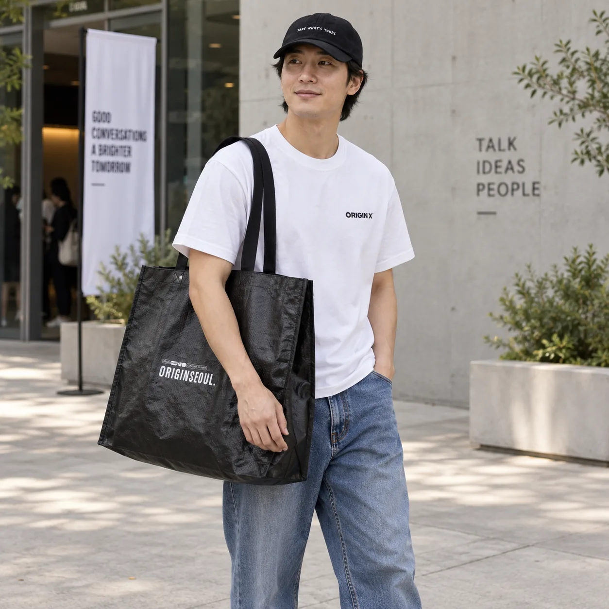 오리진X 화이트 티셔츠와 모자, 청바지 차림으로 타포린백을 어깨에 멘 사용 장면