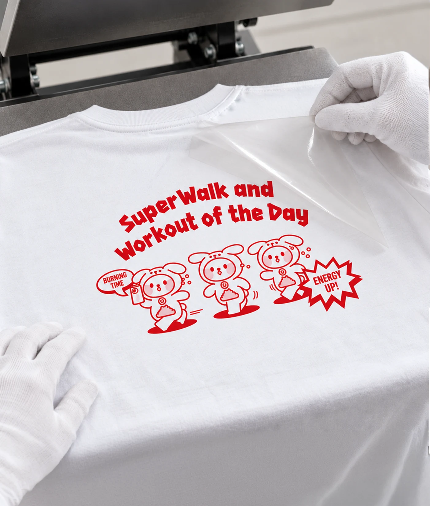 Heat transfer process: a gloved hand peels the film off after a character and lettering are transferred onto the back of a white T-shirt on a heat press