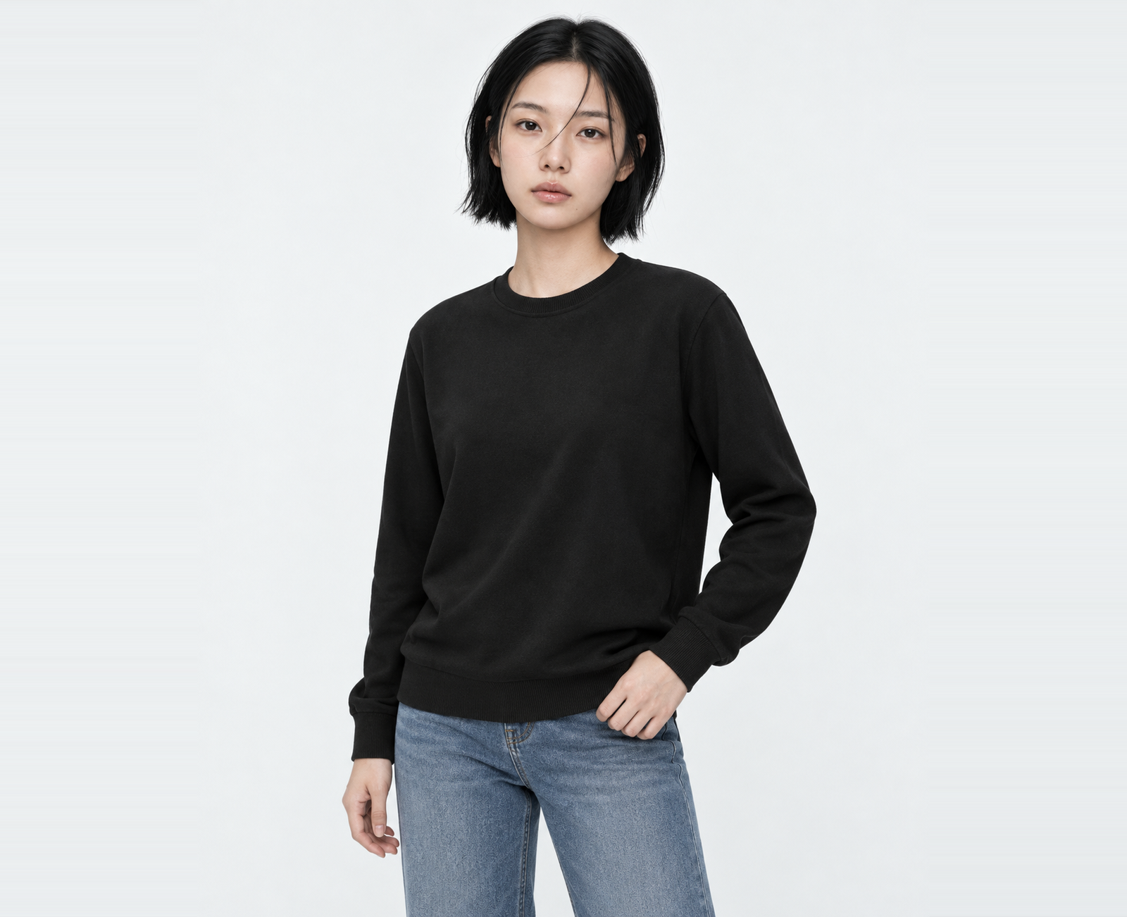 Woman wearing a black light sweatshirt in M, hand resting on the rib hem