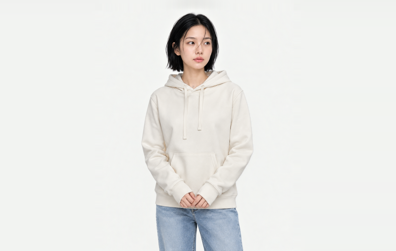 Upper body of a woman in an ivory light hoodie in M, sleeves pulled over the backs of her hands, hands together