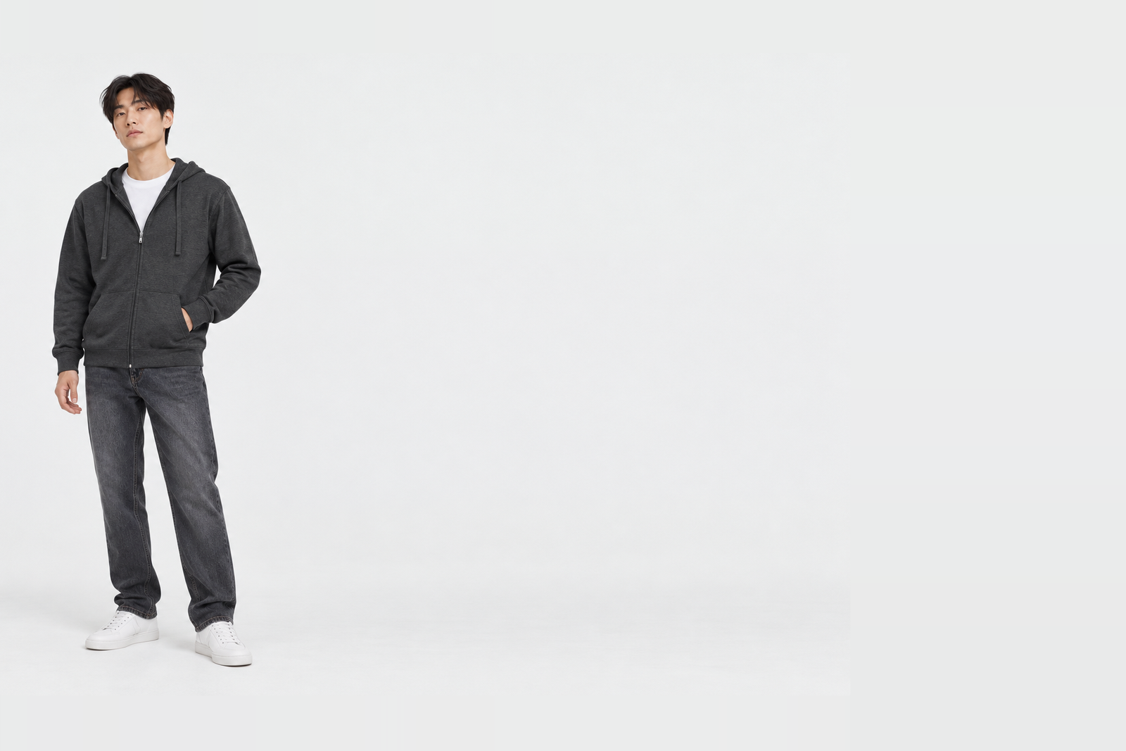 Full-length shot of a man wearing a charcoal light zip-up hoodie in XL half zipped, one hand resting in the front pocket