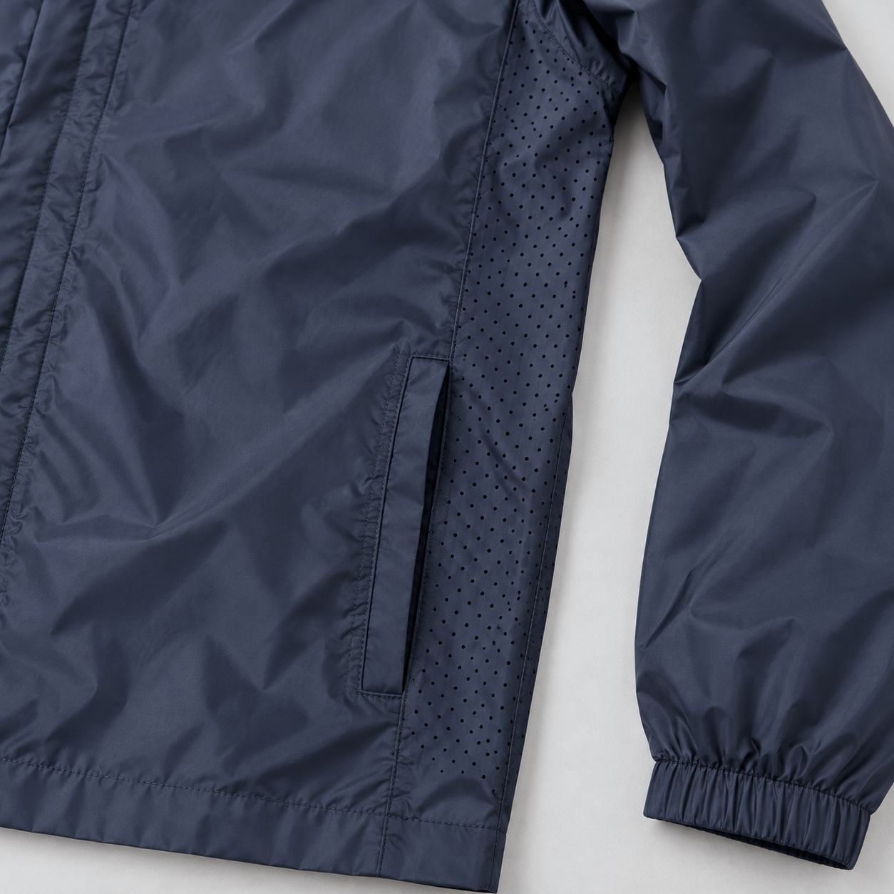 Close-up of the small ventilation holes in the side panel and the side pocket opening below on a navy windbreaker