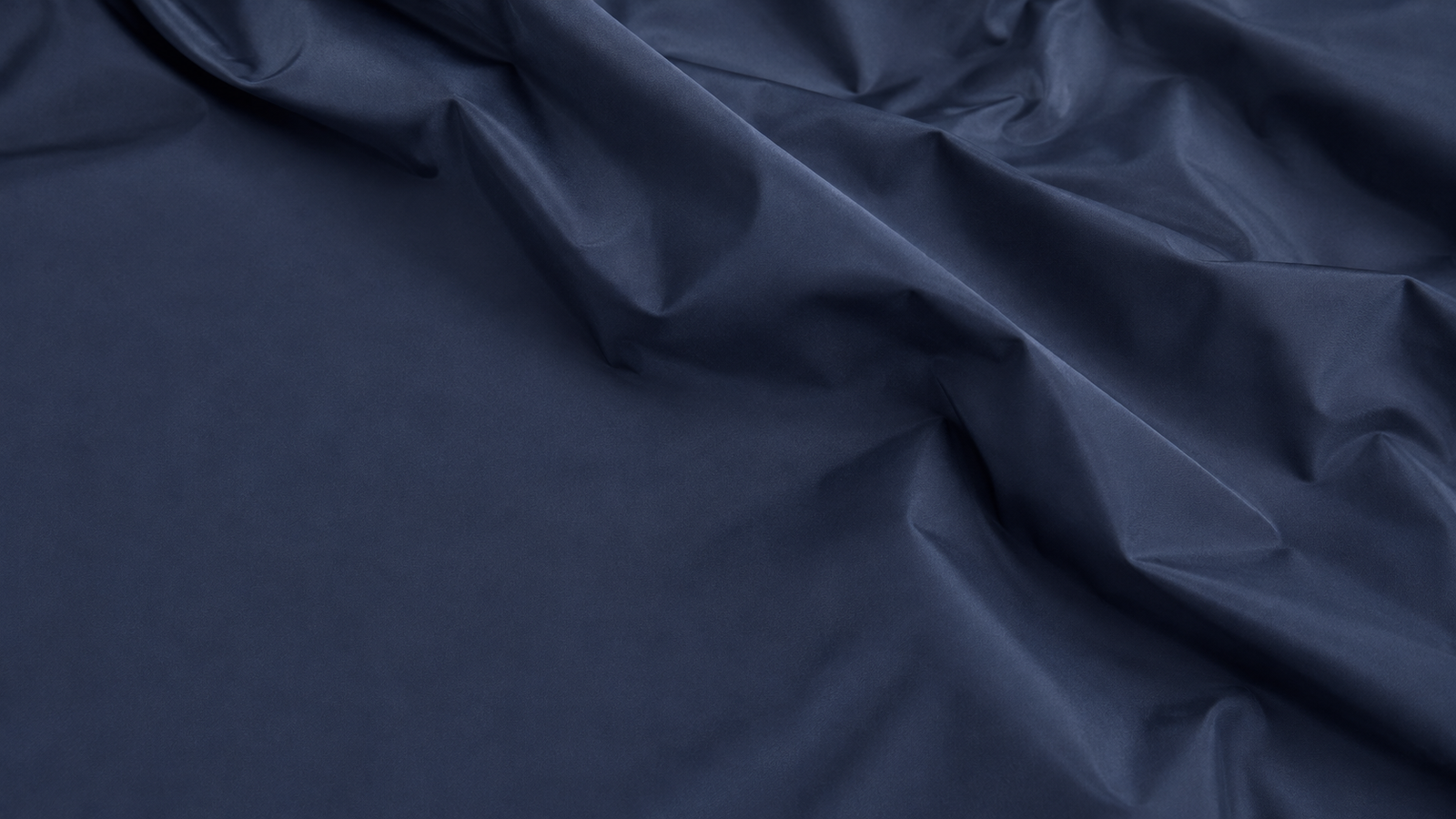 Close-up of thin navy polyester fabric loosely folded, showing the tight plain weave and a soft sheen