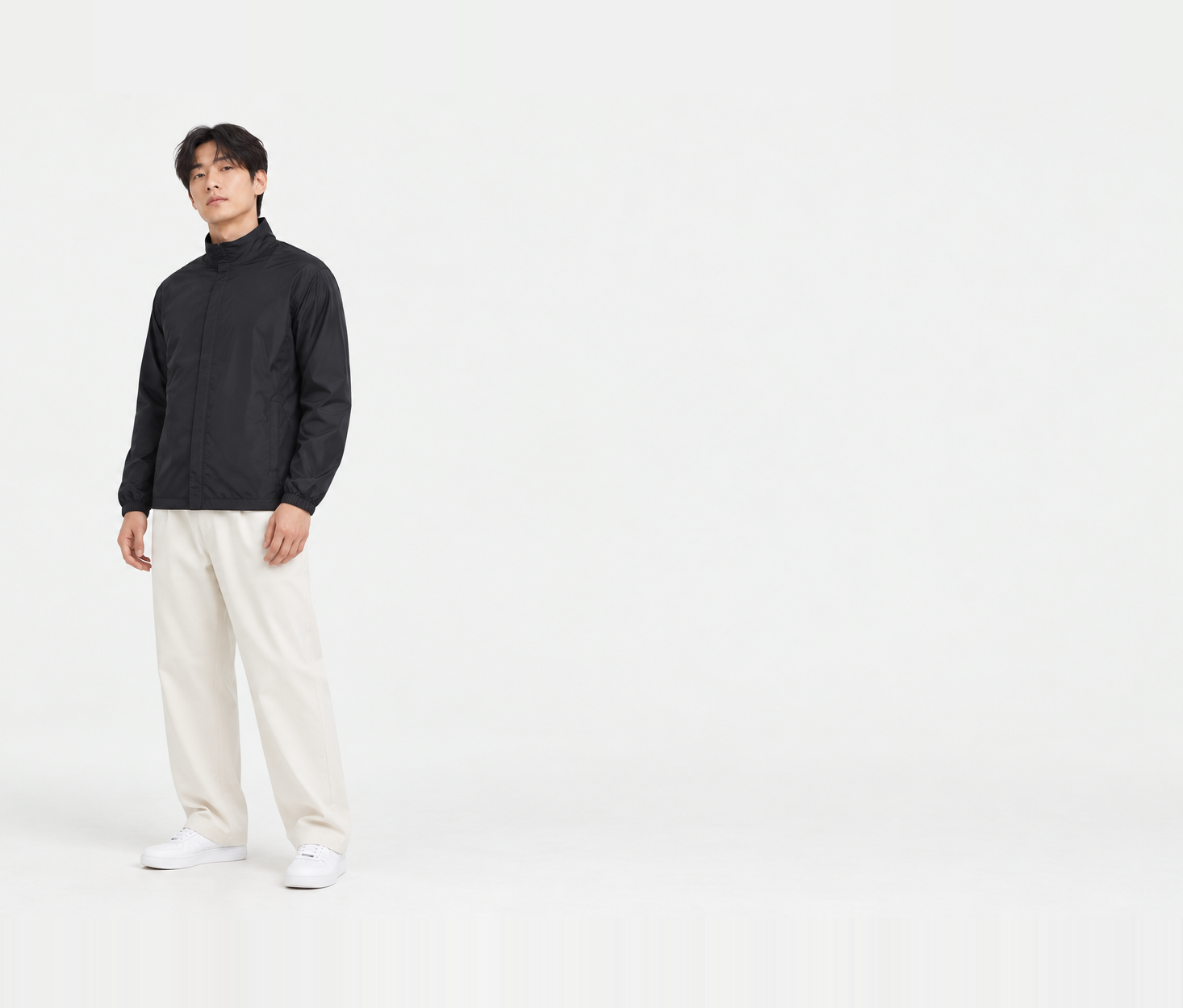 Full-length shot of a man in a black basic windbreaker in XL, standing at an angle with arms down, sleeves reaching the wrists and body length covering the waist