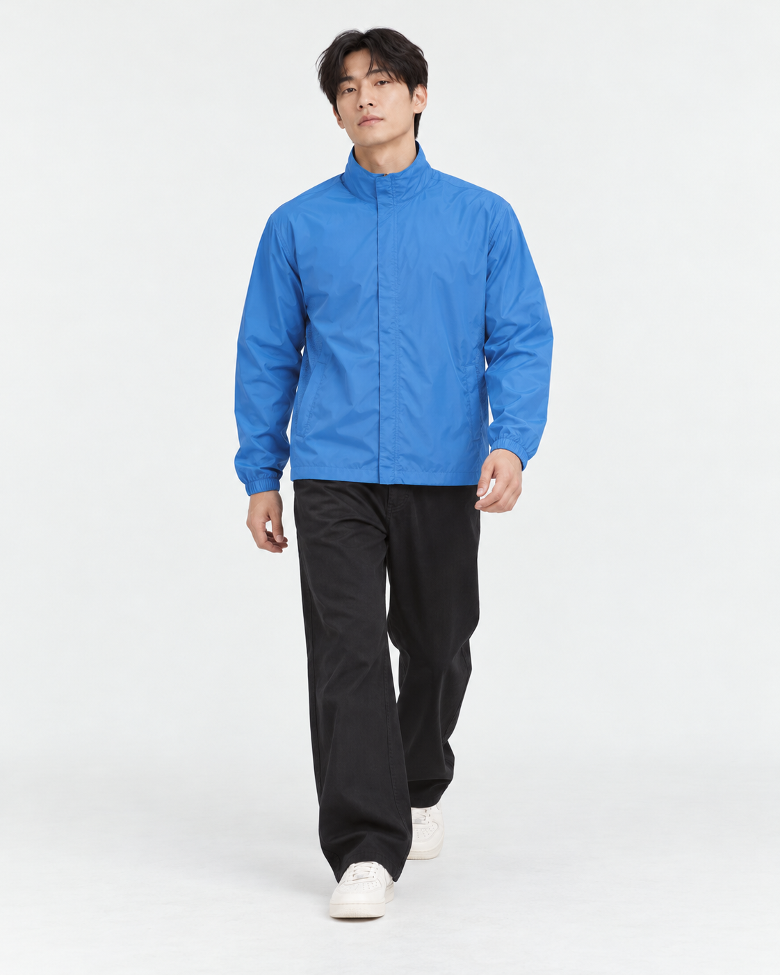 Full-length shot of a man in a blue basic windbreaker in L walking toward the camera