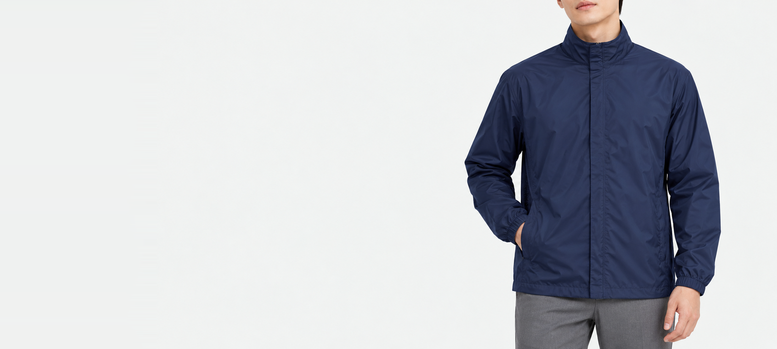 Torso of a man in a navy basic windbreaker in XL with a hand in the side pocket, showing the stand collar and elastic cuffs